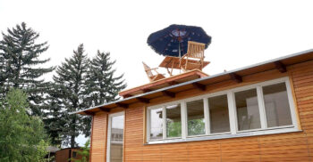 Ein Tiny Haus aus Holz mit Gartenstuehlen und einem Sonnenschirm auf dem Dach