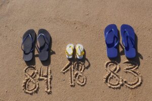 Flipflops am Strand mit Geburtsjahren im Sand während einer Reise während der Schwangerschaft