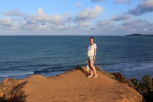 Sabine reist schwanger und steht mit Babybauch am Meer