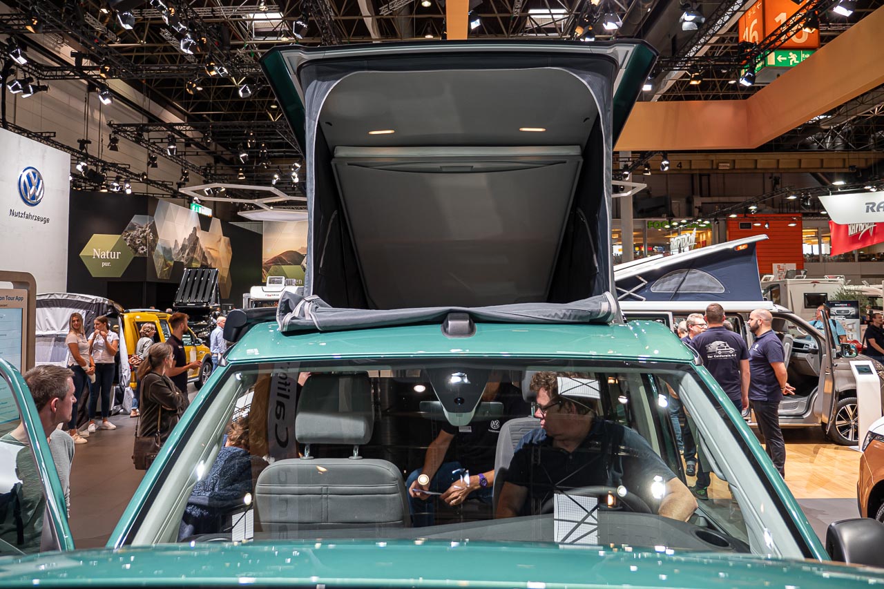 VW California 6.1 – Strand-Hopping mit Stil (inkl. Video-Roomtour) 25 Blick von vorn durch die Windschutzscheibe und auf das geöffnete Hochdach eines VW California 6.1 Coast auf dem Messestand des Caravan Salon 2019 in Düsseldorf