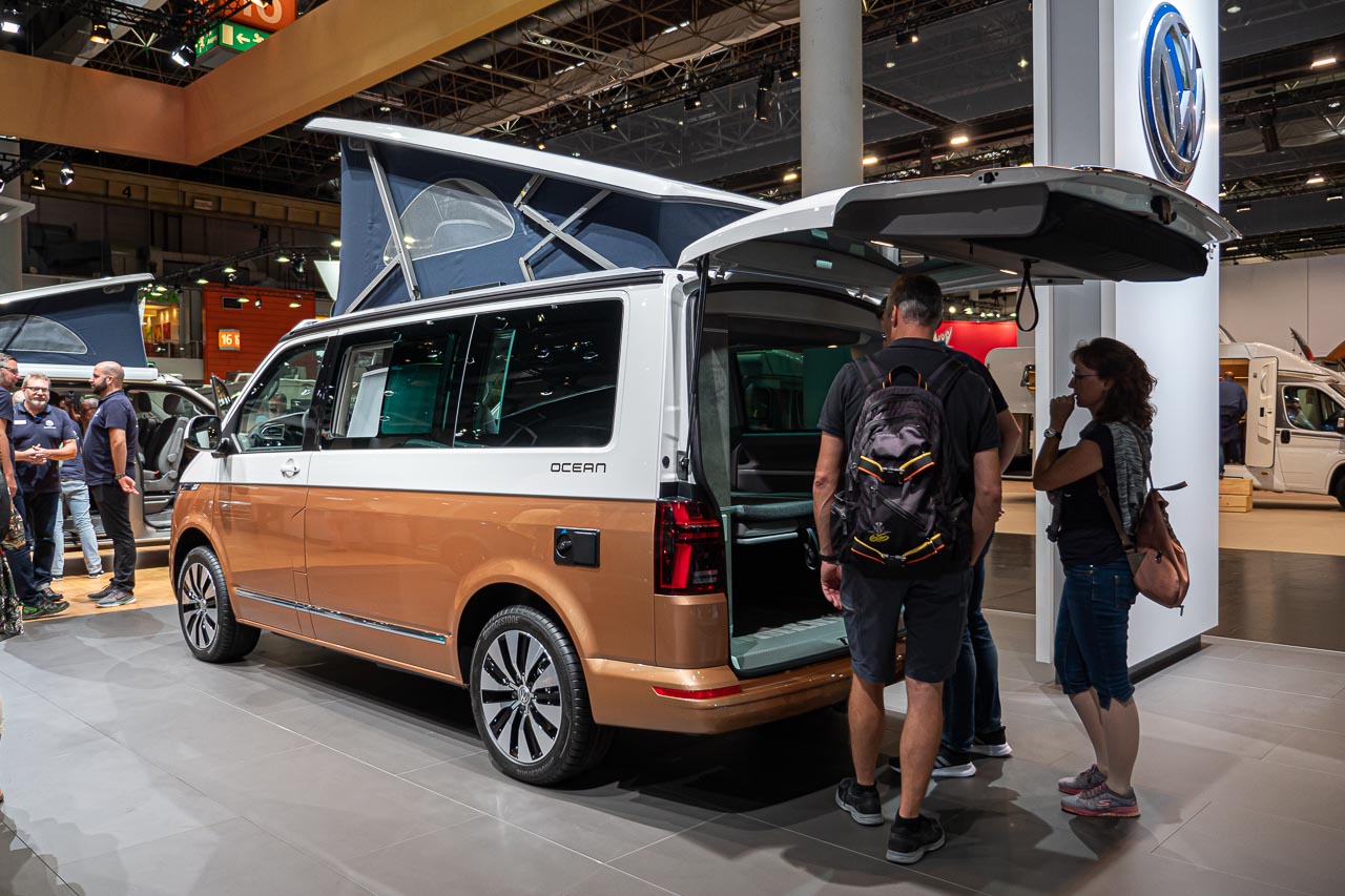 VW California 6.1 – Strand-Hopping mit Stil (inkl. Video-Roomtour) 3 Blick von der Seite auf einen VW California 6.1 Ocean mit offener Heckklappe und aufgestelltem Hochdach auf dem Messestand des Caravan Salon 2019 in Düsseldorf