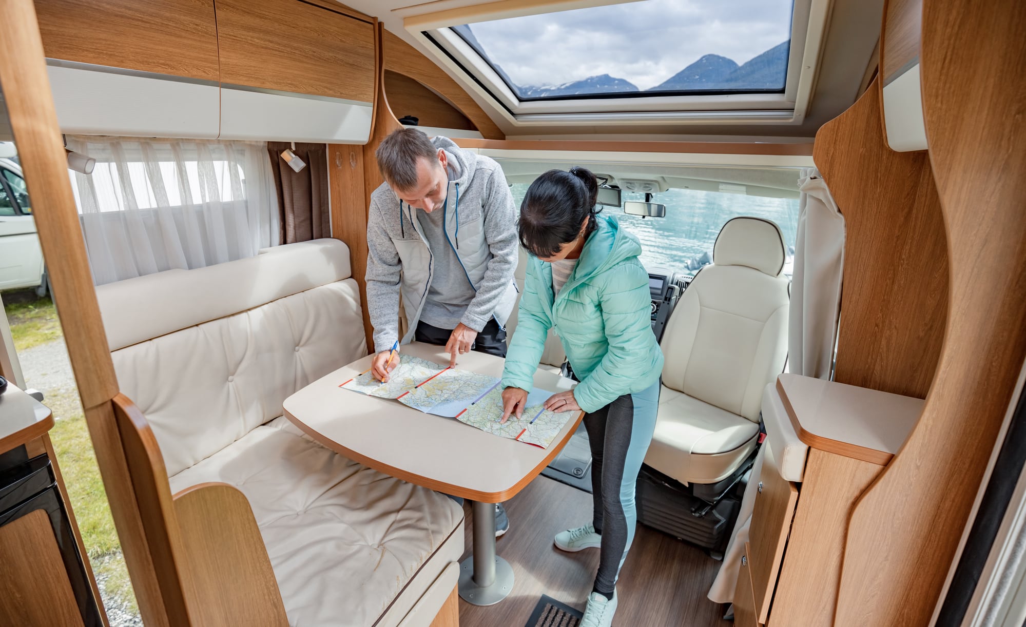 Paar steht im Wohnmobil am Tisch und schaut auf eine Landkarte