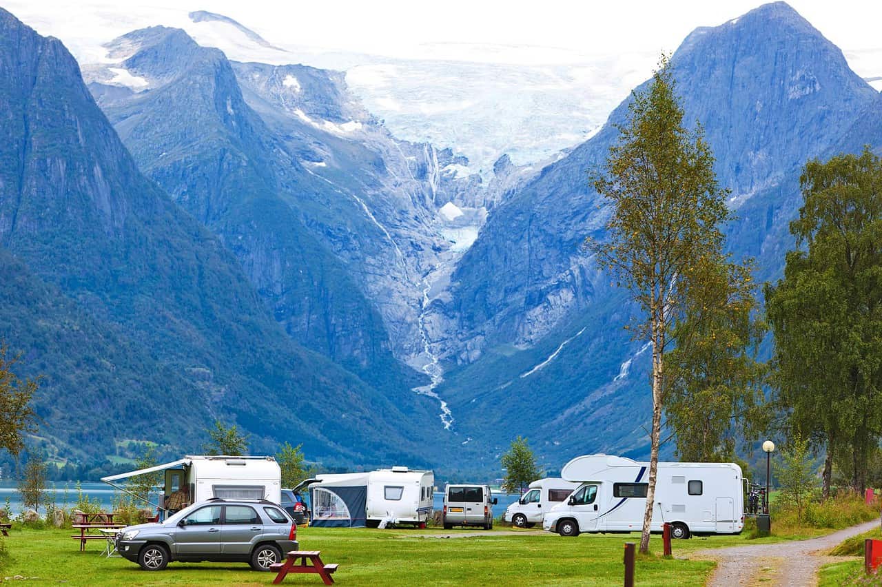 Helle Wohnmobile und Zelte am malerischen Fjord, umgeben von Bergen und Natur. Perfekt für Camping und Outdoor-Abenteuer in Norwegen.