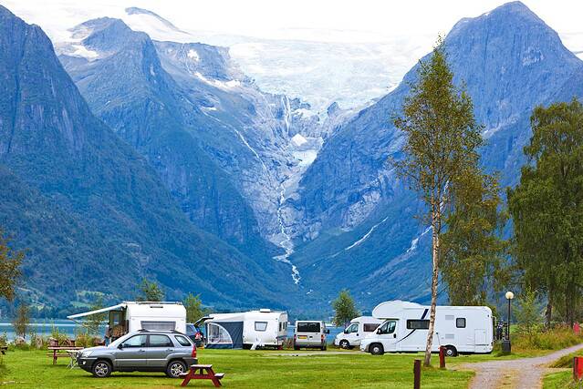 Helle Wohnmobile und Zelte am malerischen Fjord, umgeben von Bergen und Natur. Perfekt für Camping und Outdoor-Abenteuer in Norwegen.